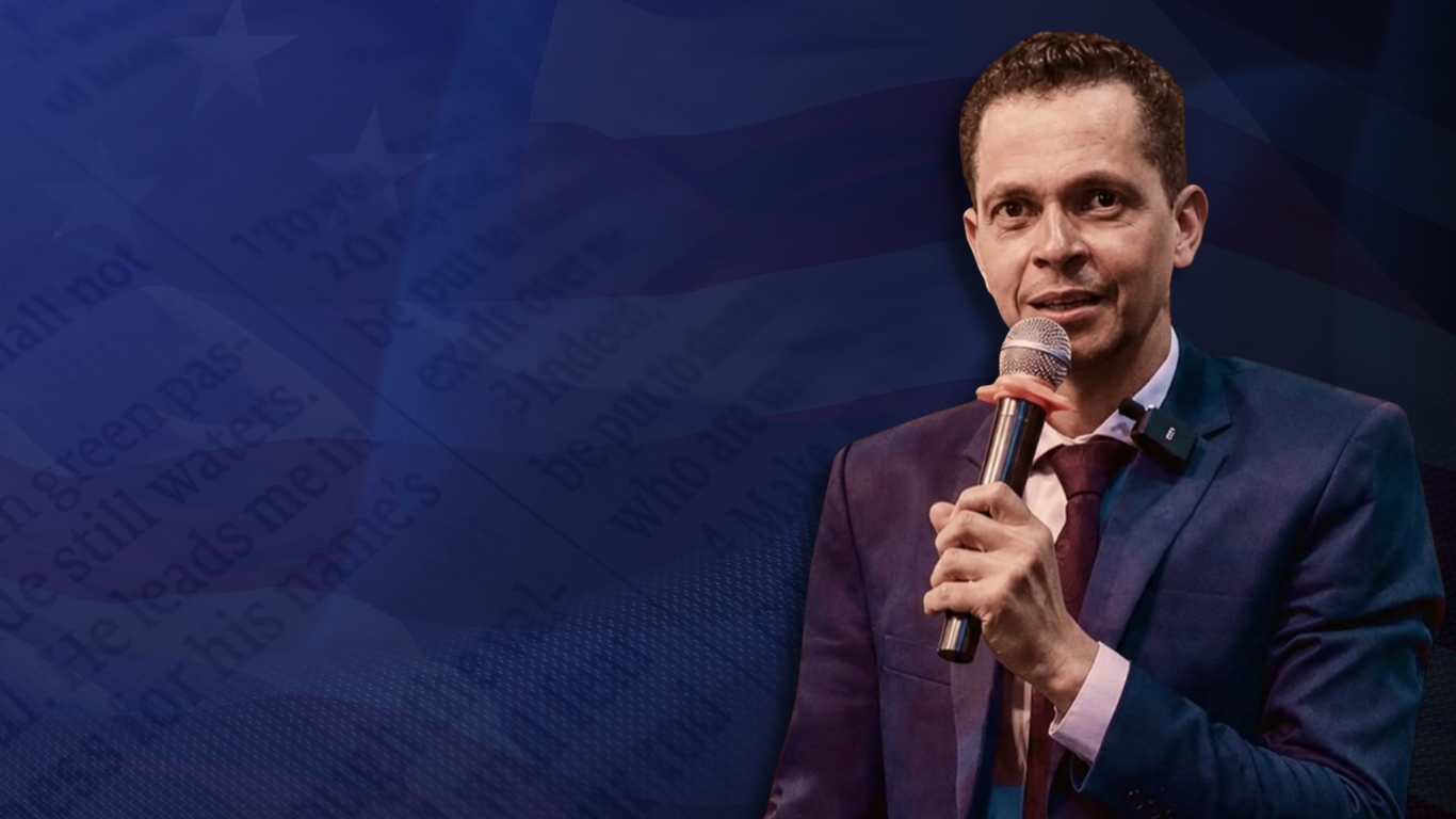 Pr. Leone Passos com microfone diante de uma composição em azul profundo